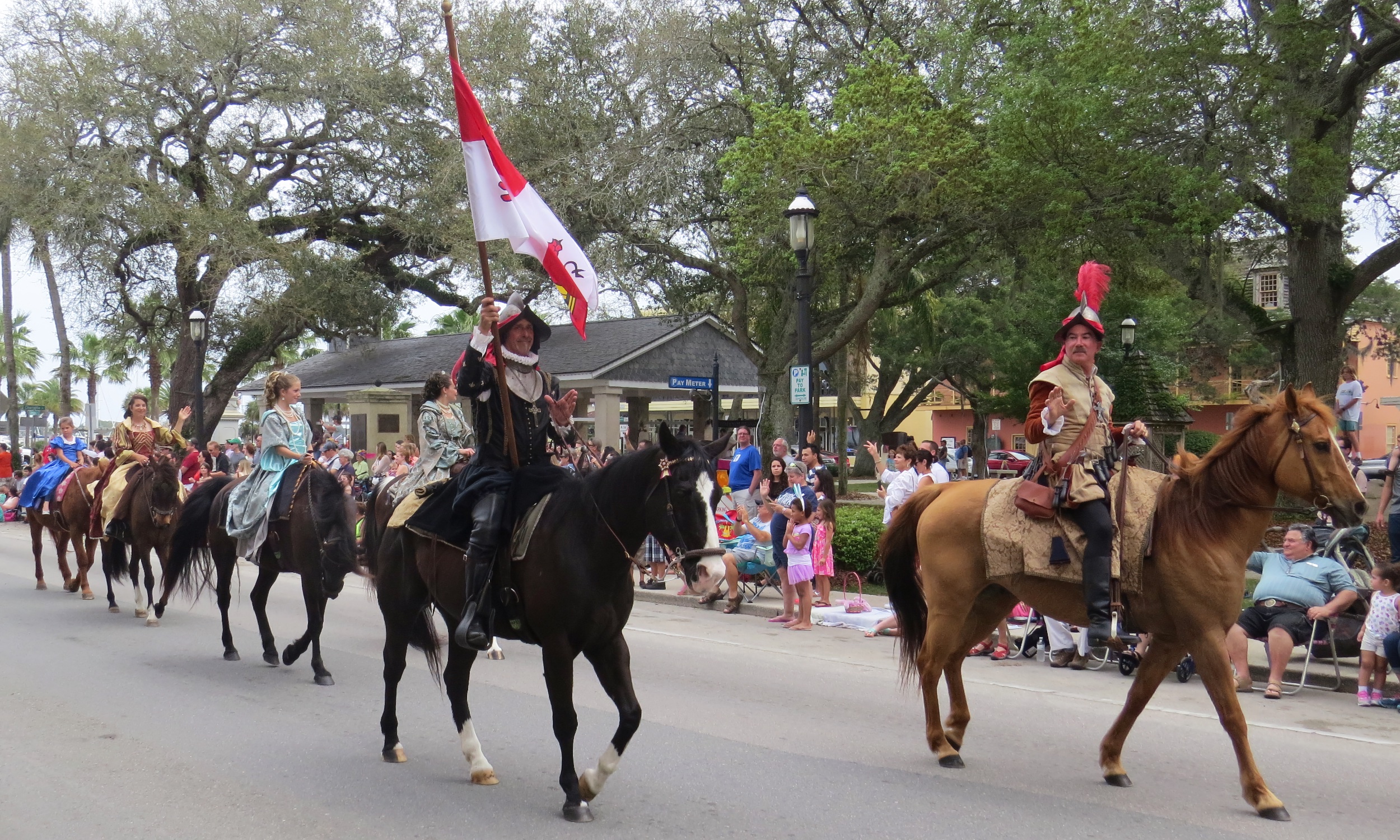 Members of the Royal Family lead the parade on horseback, flying the Spanish flag