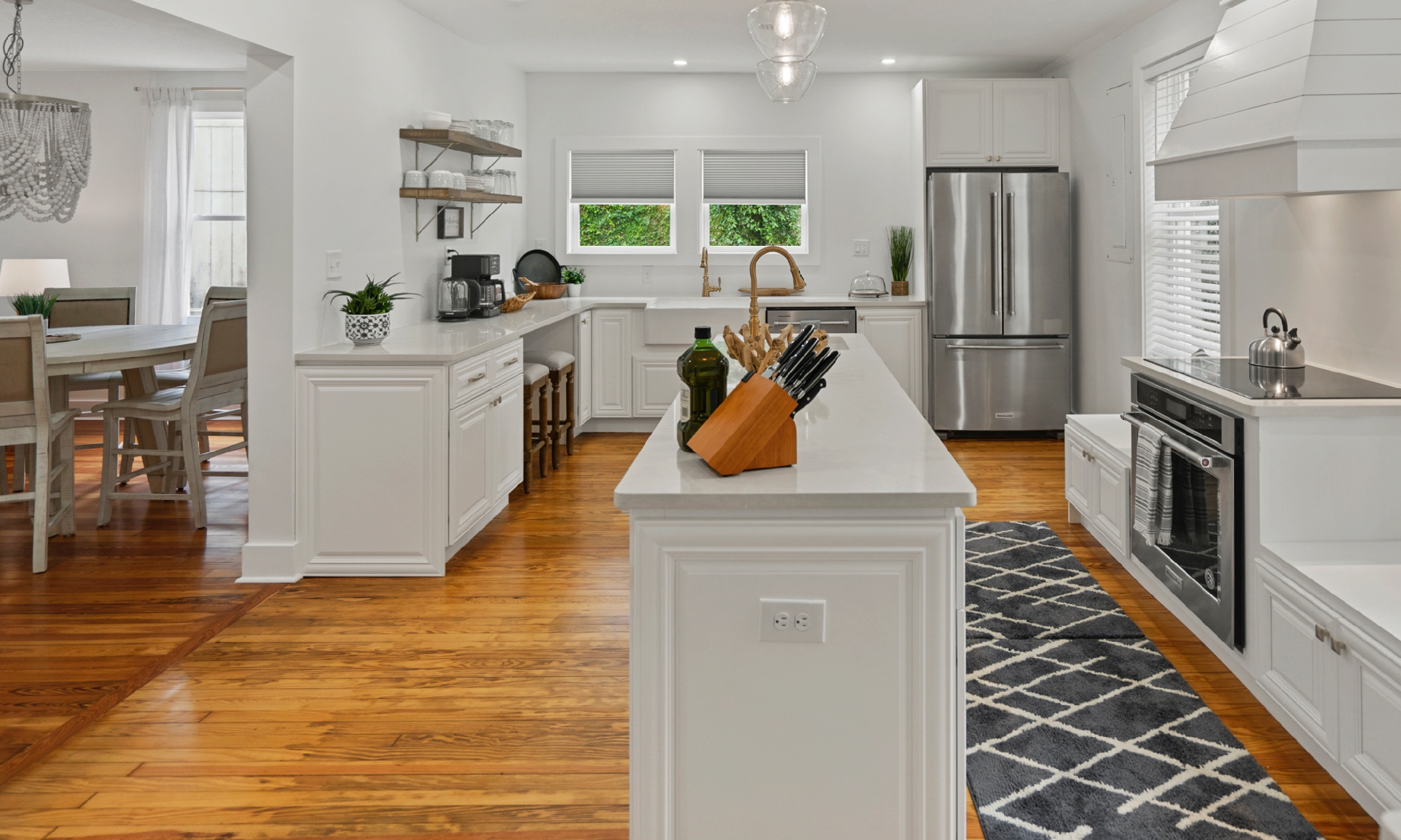A large kitchen, in white, opens to a diningroom, both with natural wood floors