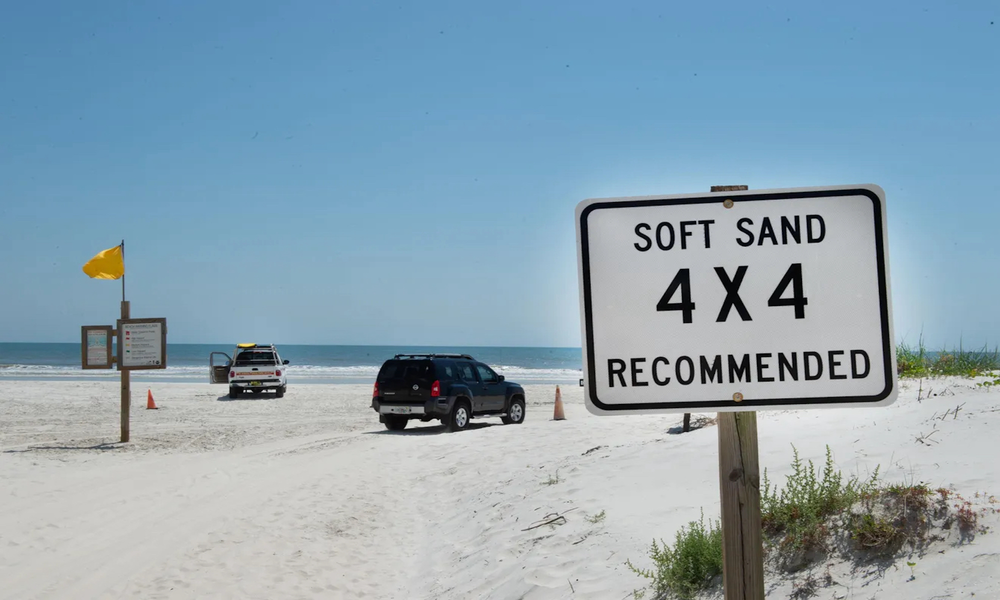 A 4x4 warning sign with SUVs parked on Crescent Beach