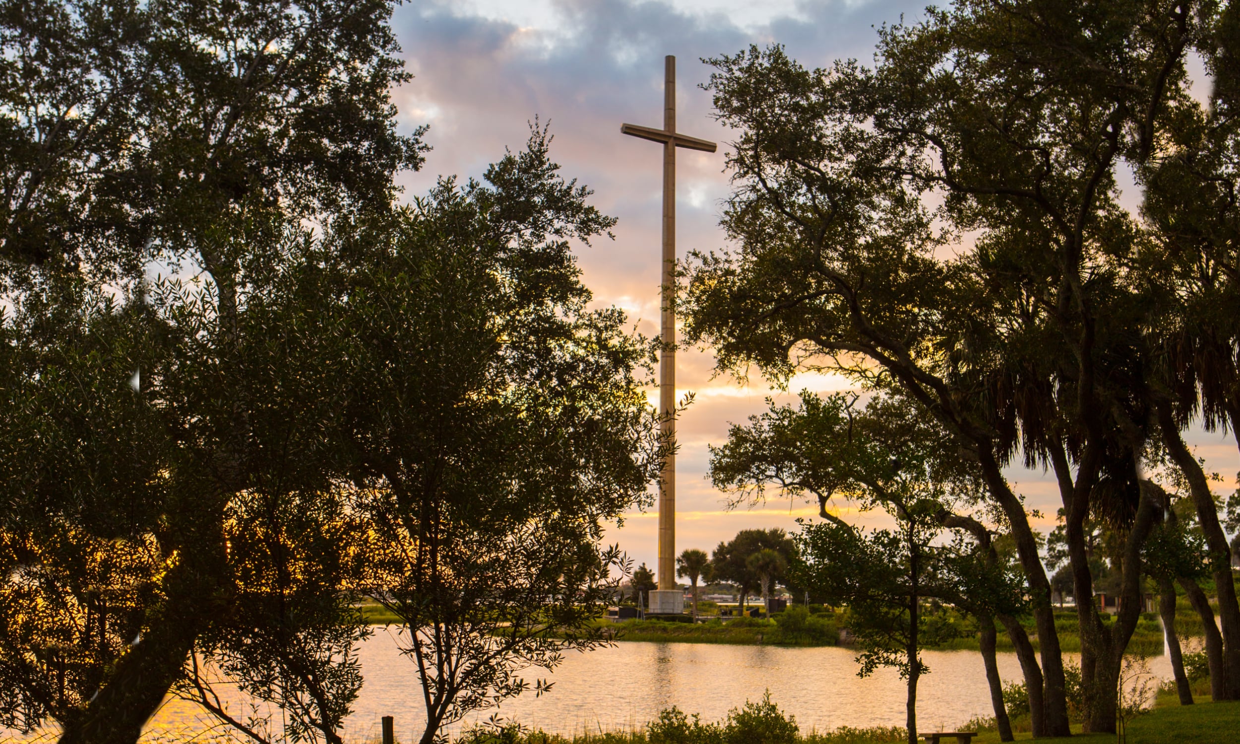 Through silhouetted live oaks, a sunset reflects on the Matanzas River, above which the Great Cross towers, 68 ft total.