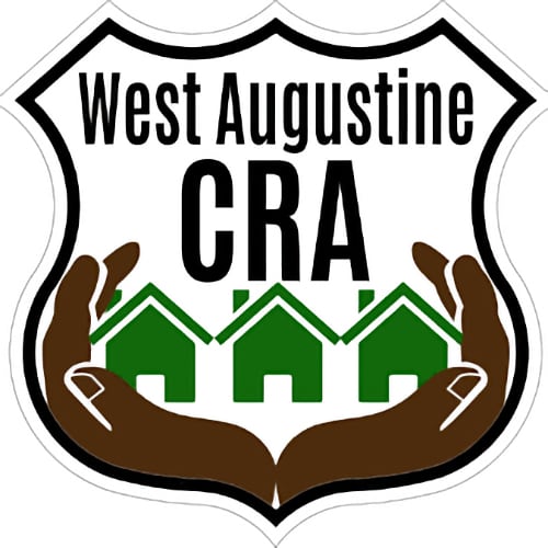 Shield shaped logo of the West Augustine CRA, which shows a pair of dark brown hands cradling three green homes.