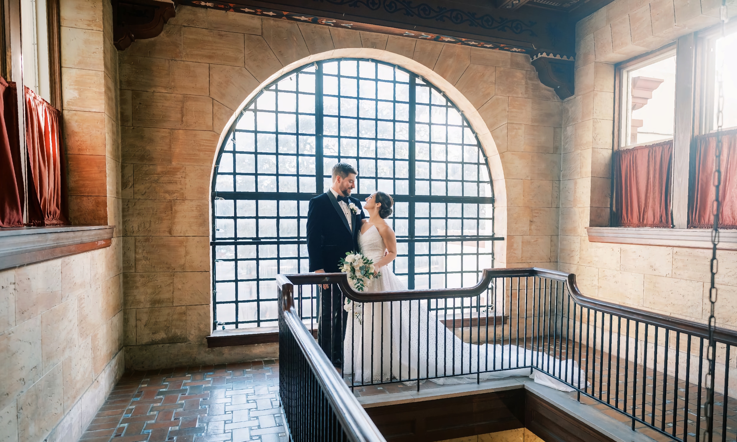 A bride and groom standing at the arched window one the balcony at Treasury on the Plaza