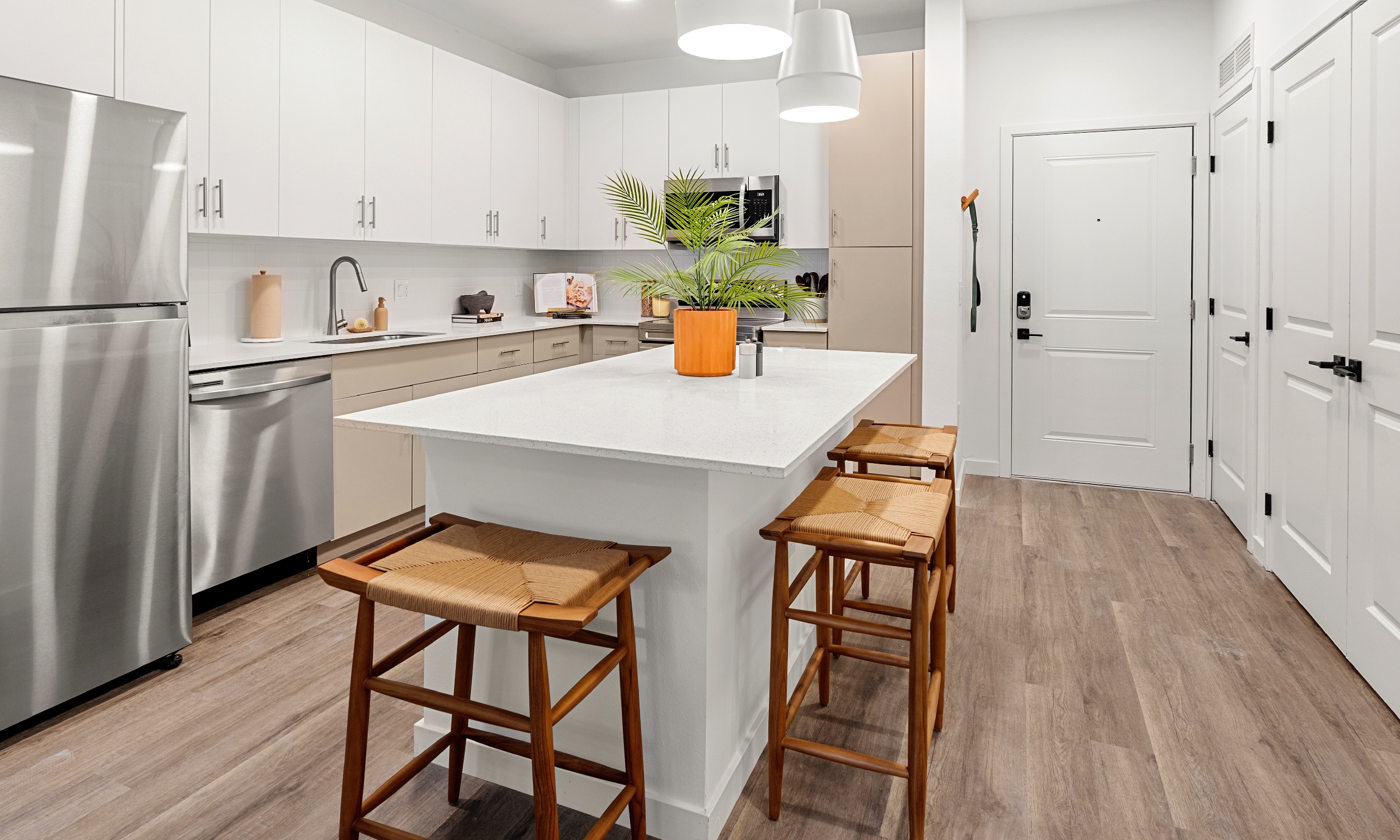 A new apartment kitchen with stainless appliances, white counters and a center island with stools