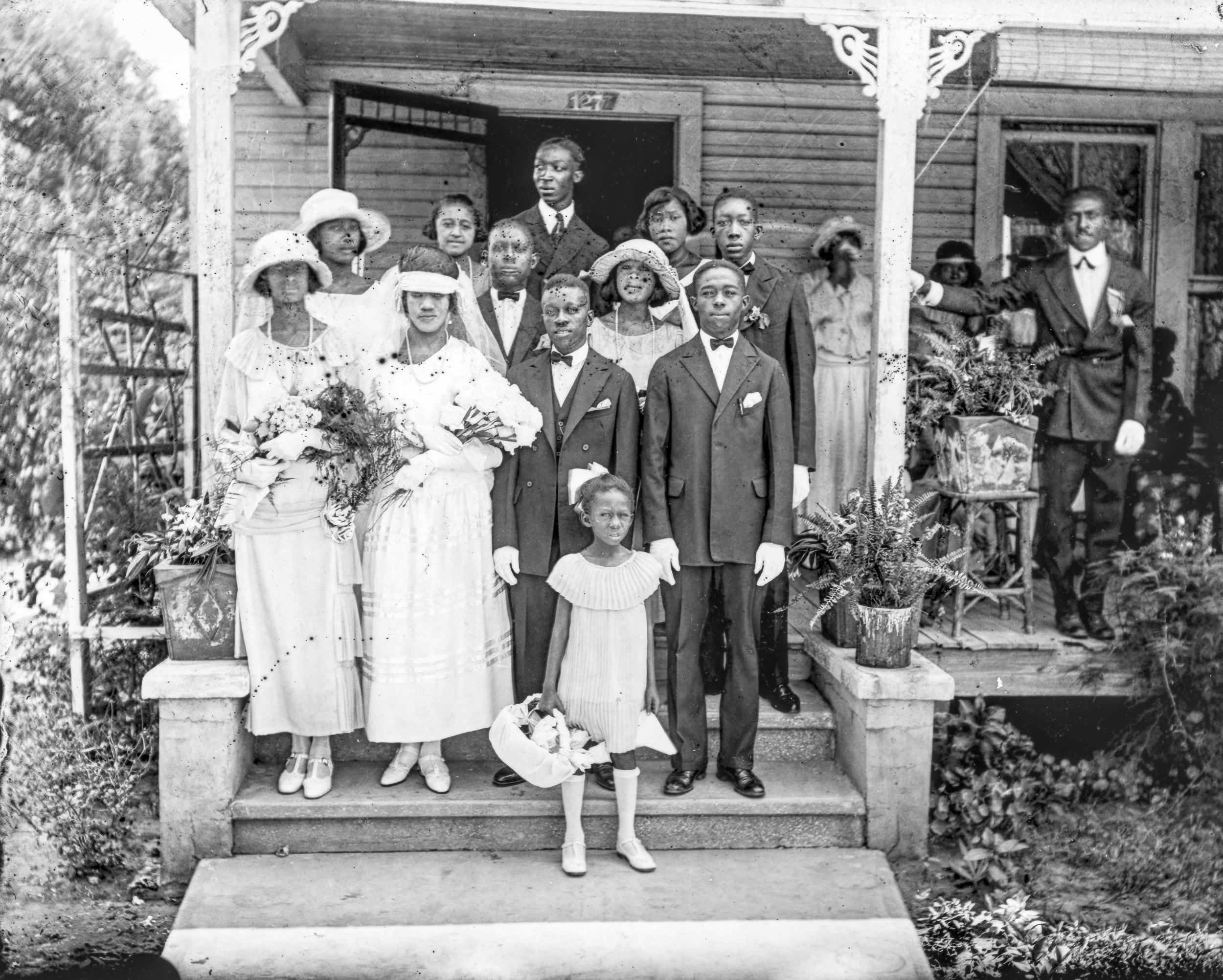 B&W, a wedding party of 20 or so people stand on the front porch of a Victorian house in Lincolnville. 