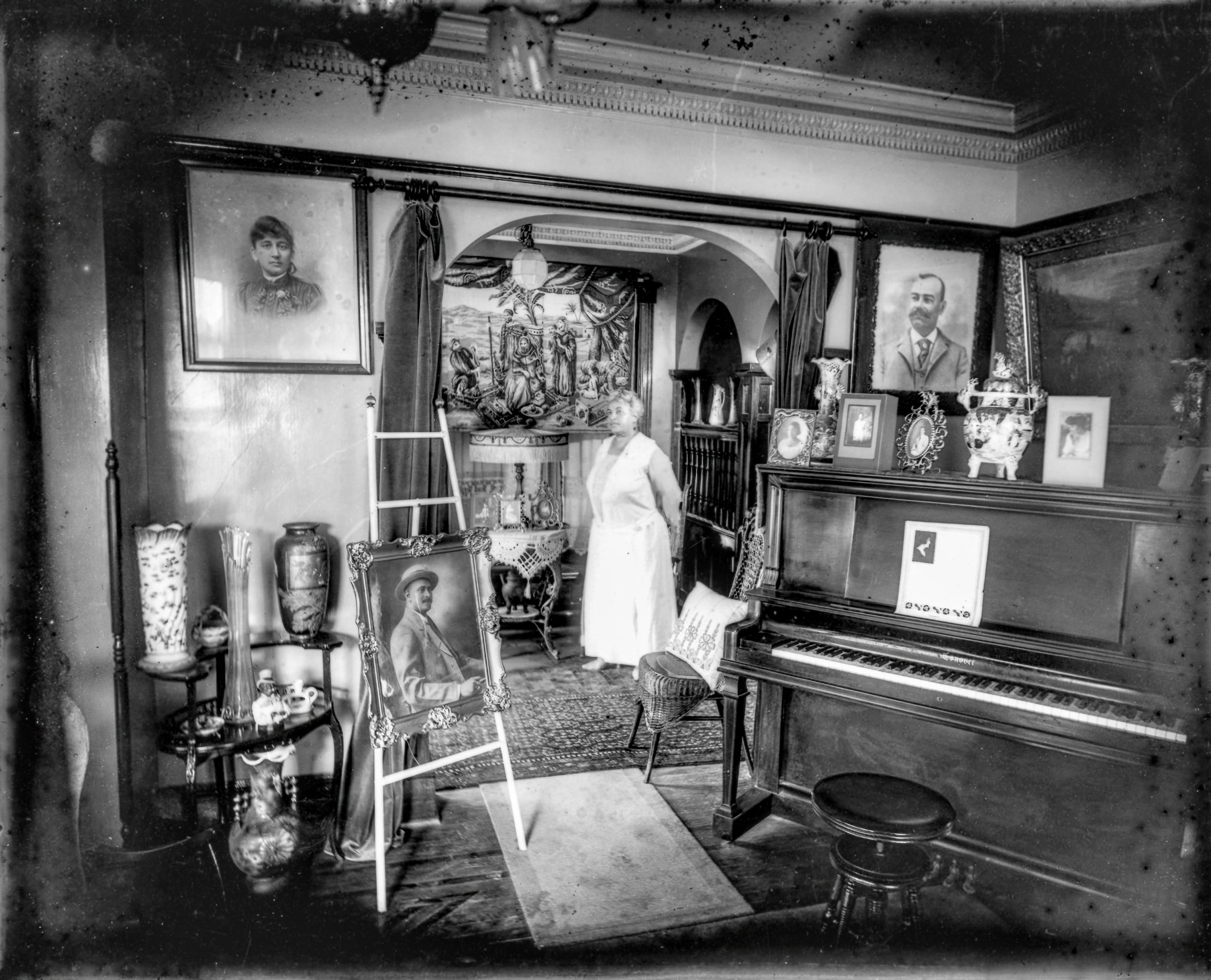 B&W, an older Black woman dressed all in white poses amongst her opulent parlor.