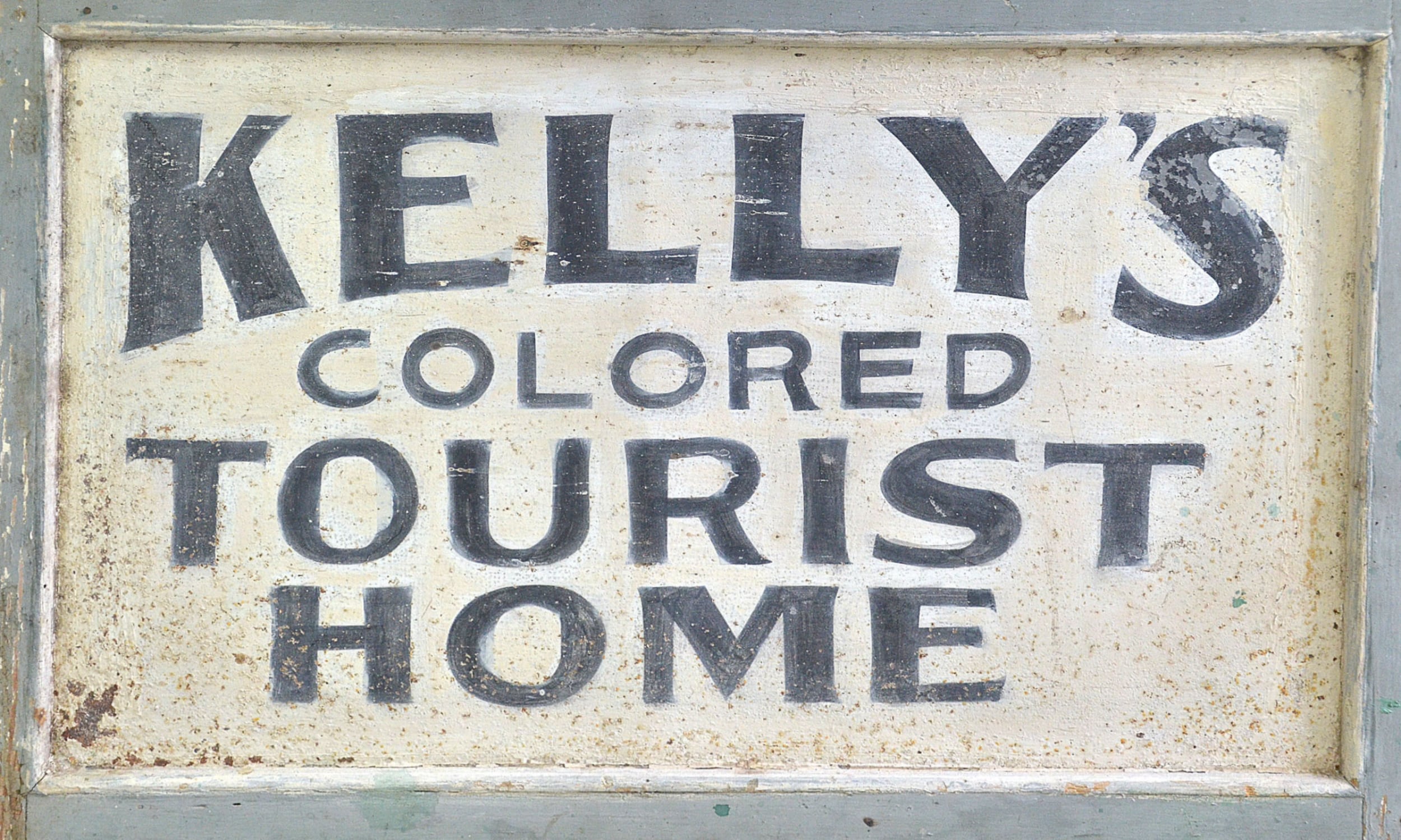 Painted old time sign that reads "KELLY'S COLORED TOURIST HOME" in painted black letters.