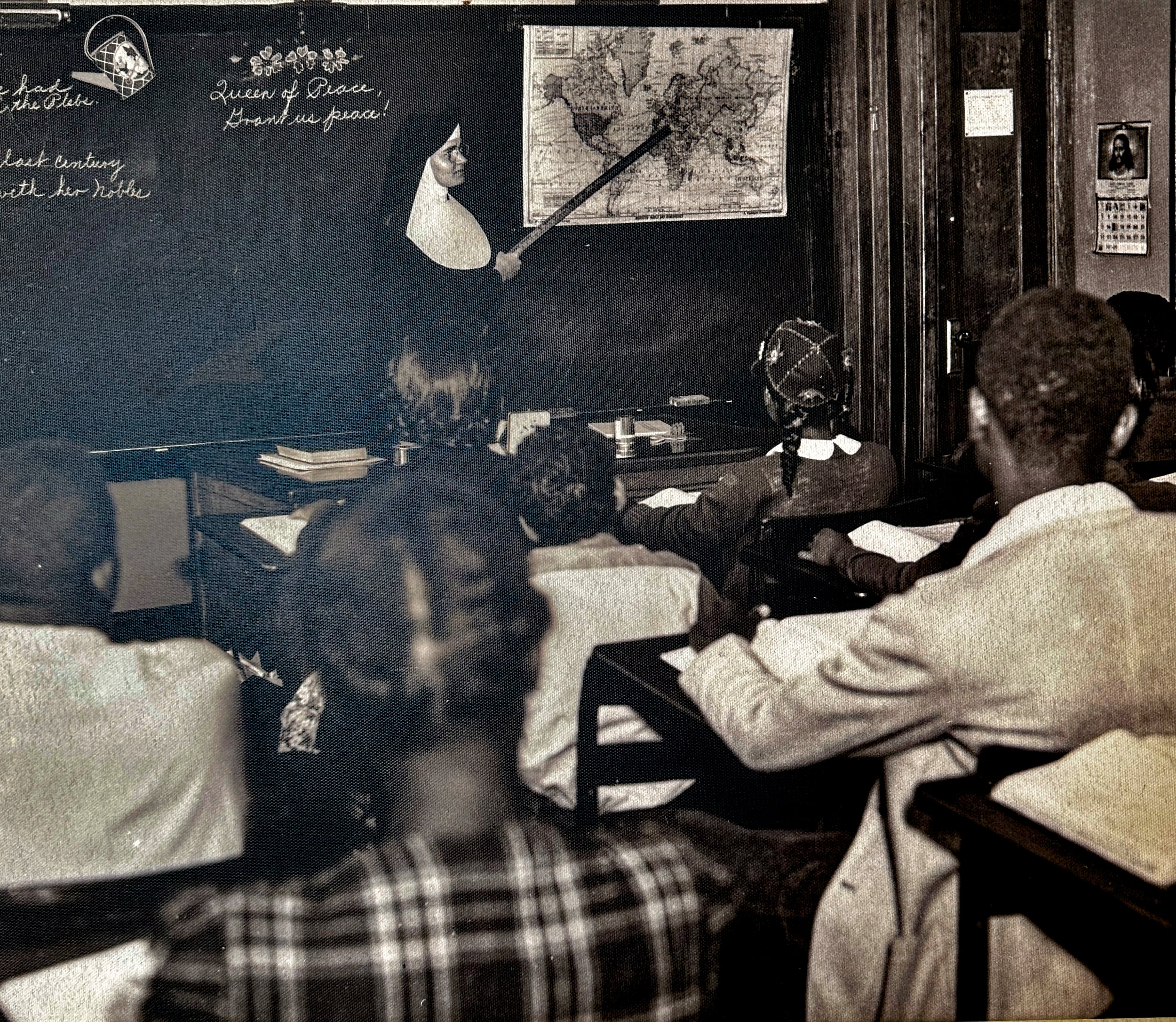 B&W, a group of students from behind, watch their teacher (a Sister of St. Joseph) point at a world map hanging over the blackboard.