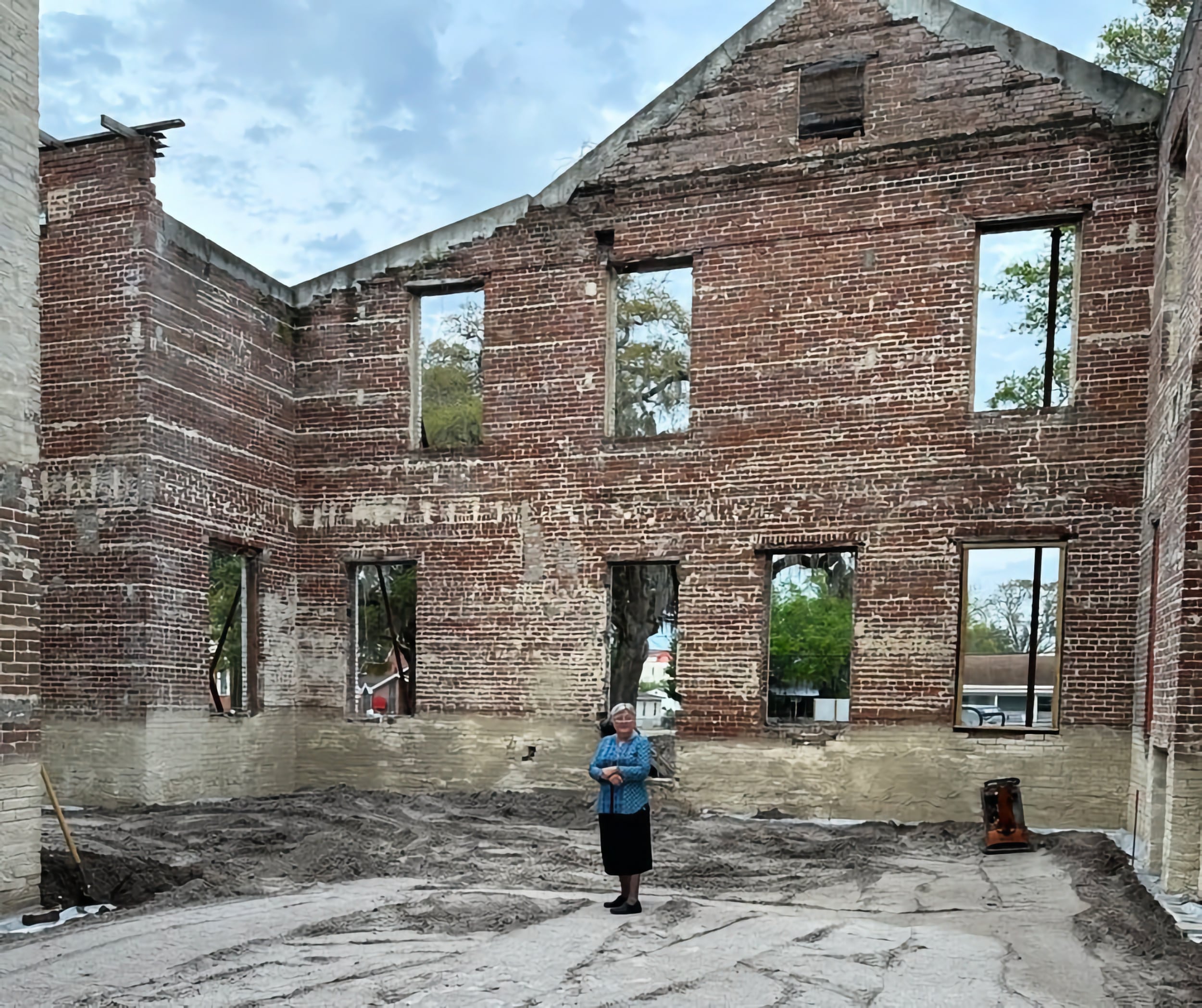 An older lady (Sister of St. Joseph) stands among the bare brick walls of 86 M.L. King Ave, the St. Joseph Neighborhood Center.