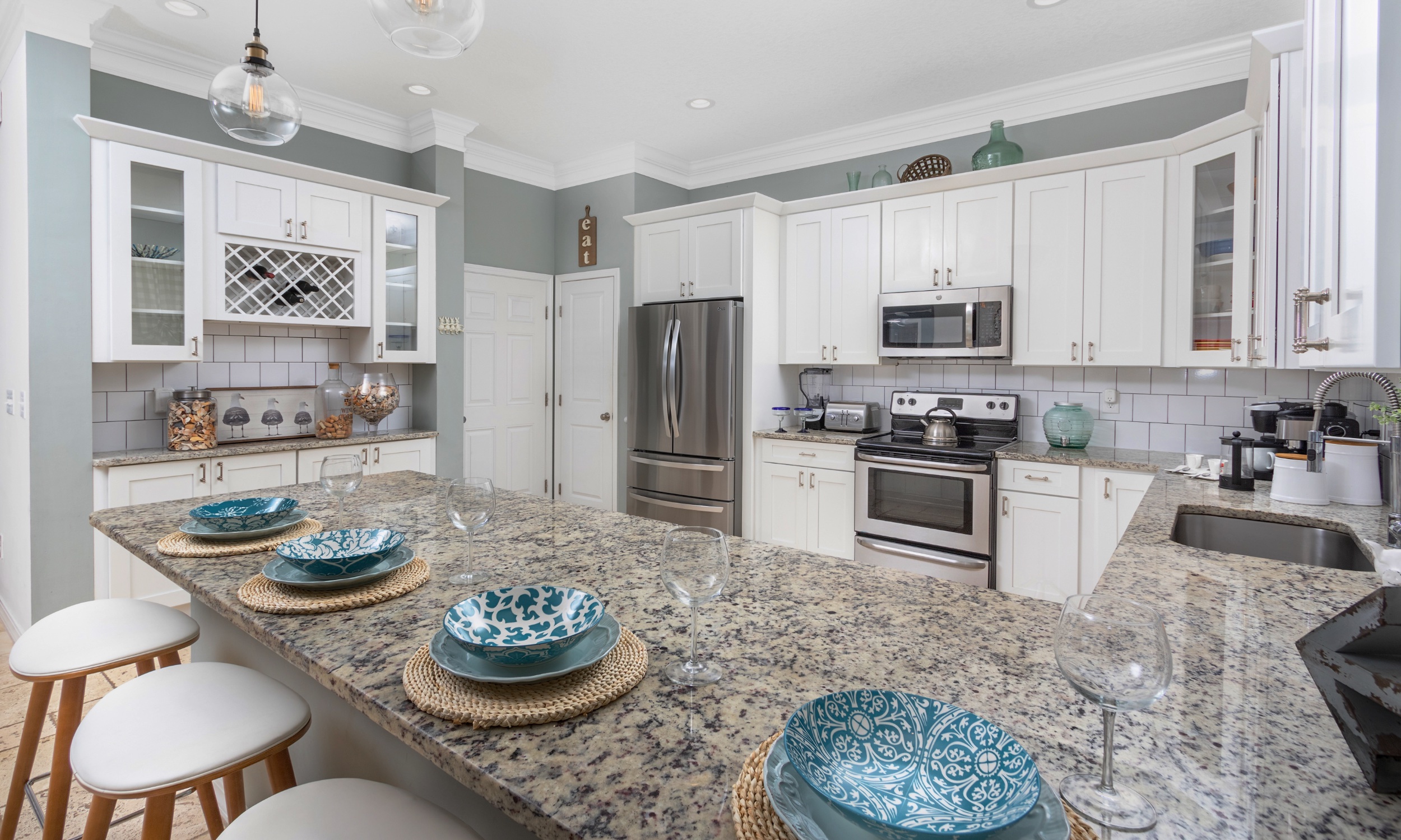 This kitchen has granite counters, a white and grey decor, and colorful dishware on an eat-in island