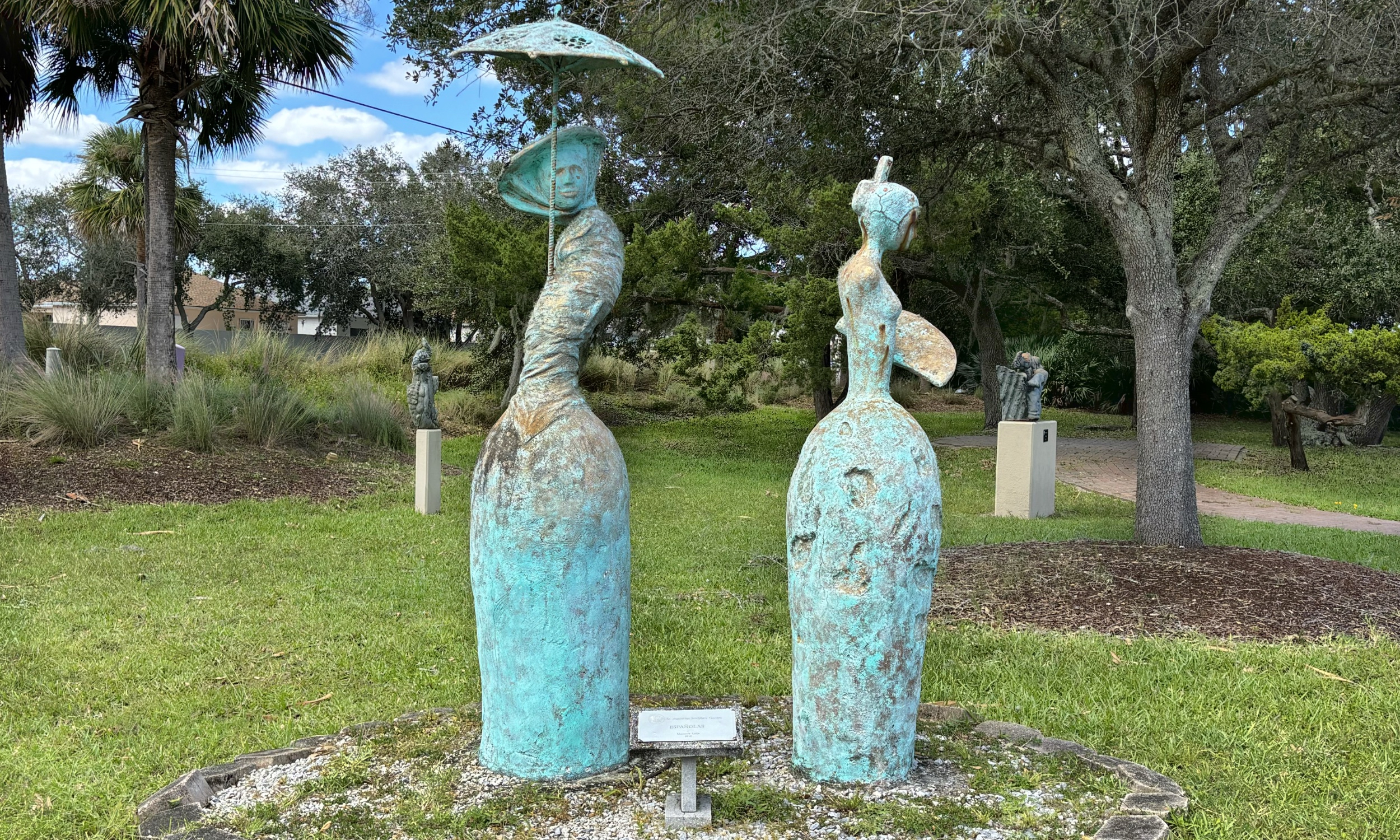 A sculpture of two women in long dresses on display in the park