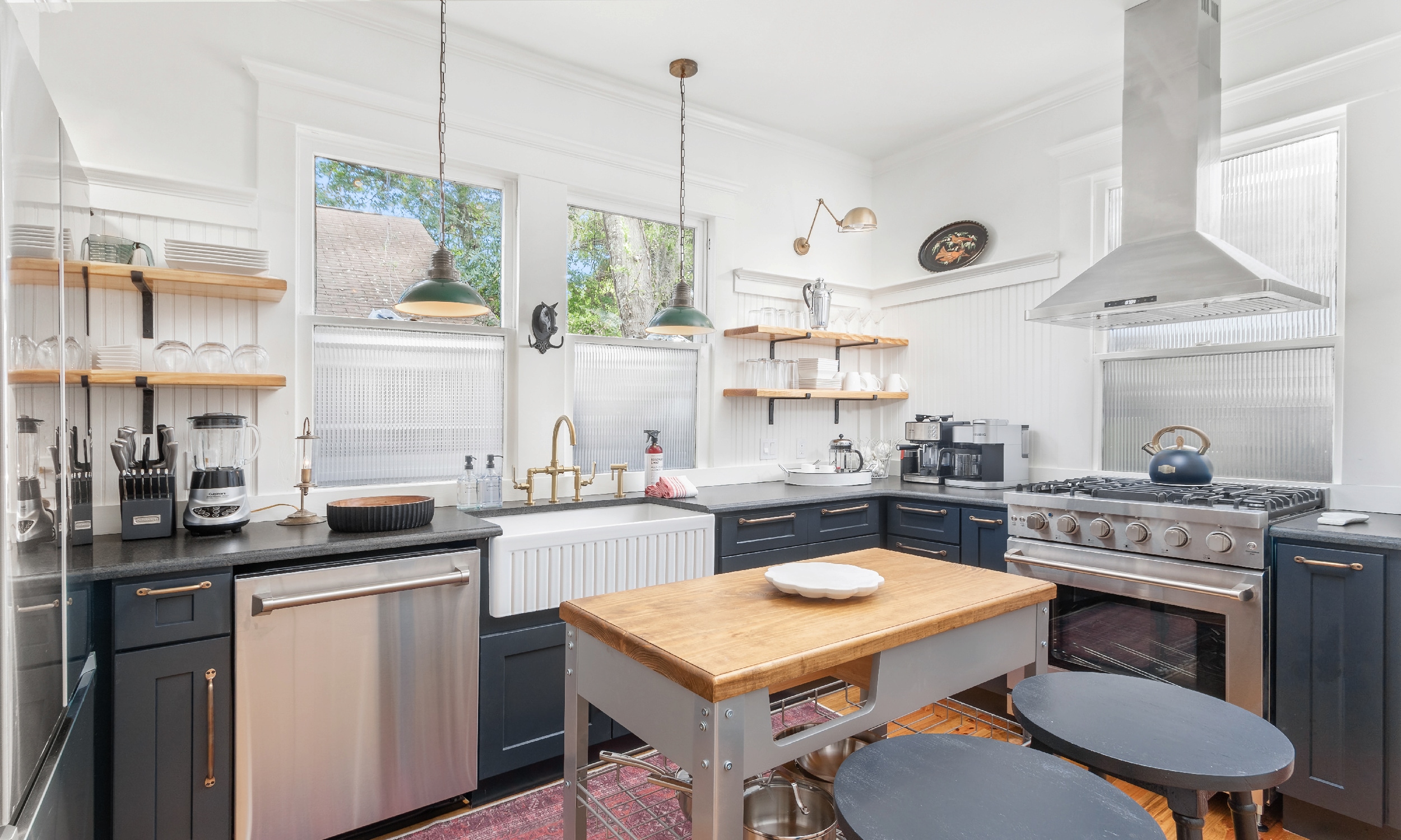 The chef's kitchen in a vacation rental has an island, large gas range, and open shelving