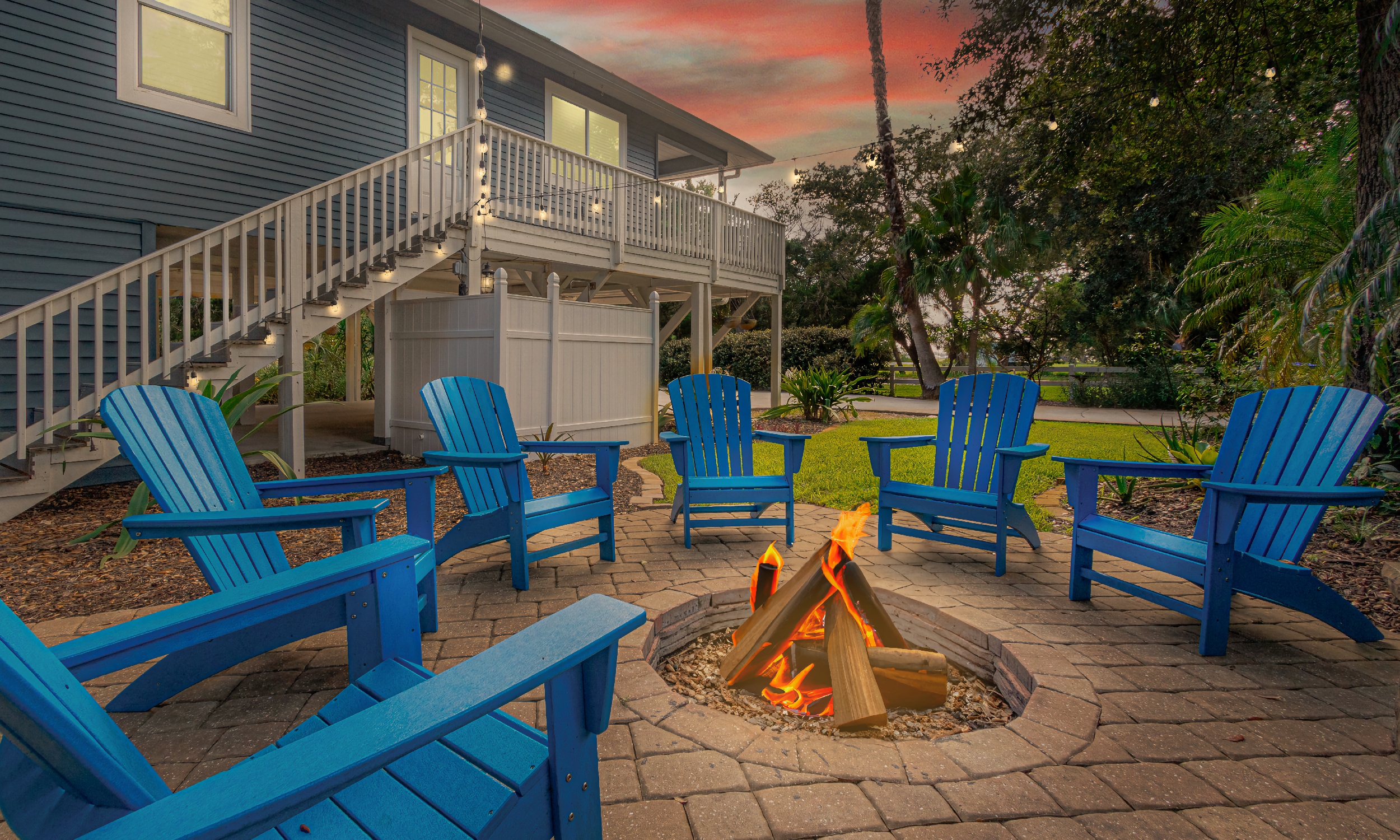 Six blue Adirondack chairs around a back-yard fire pit with burning logs