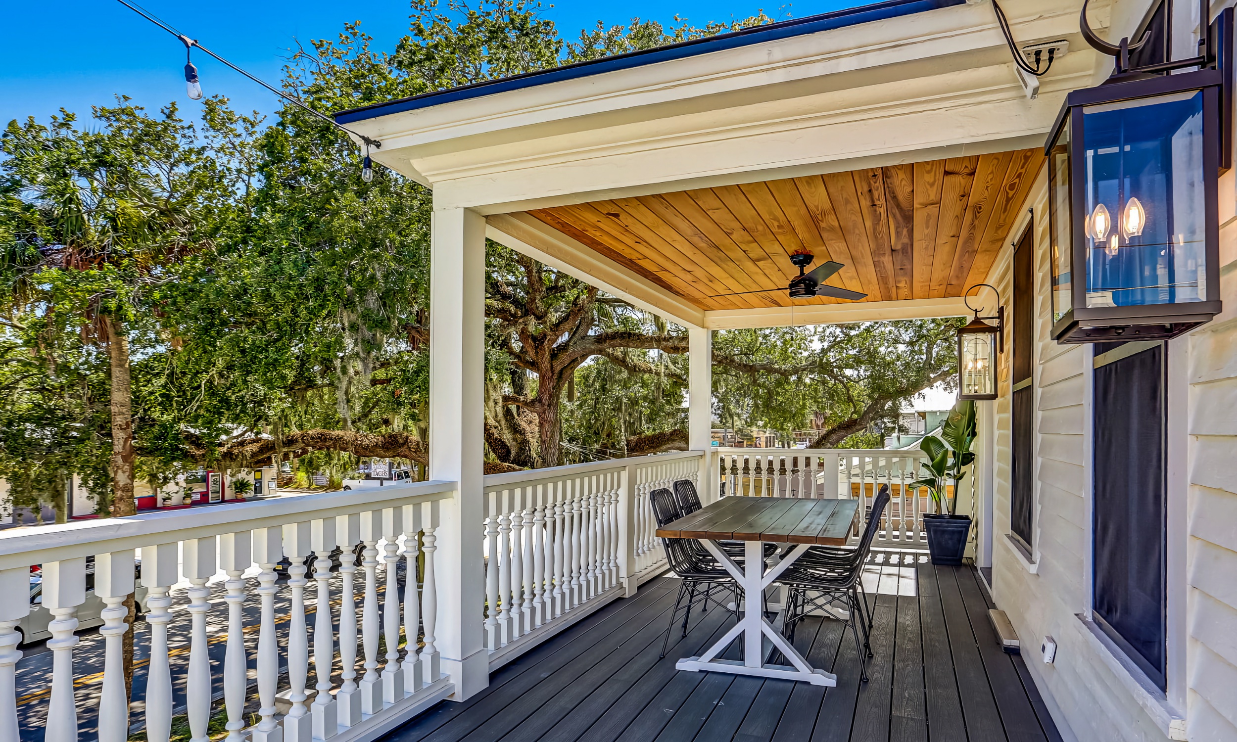 This long deck has a white railing and a wooden ceiling over the table