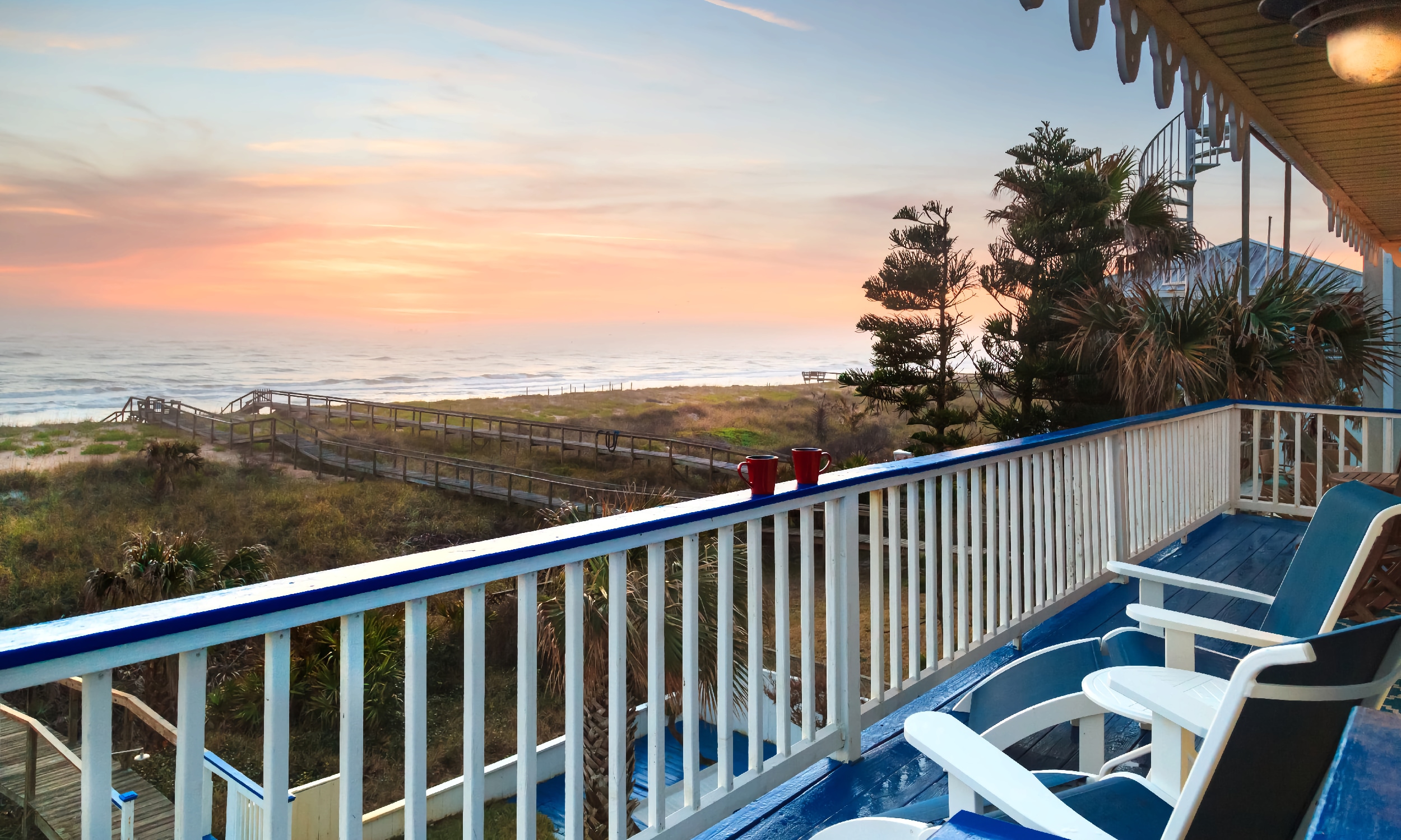 A deck with a blue floor and rail, white spindles, blue and white furniture, and an ocean view