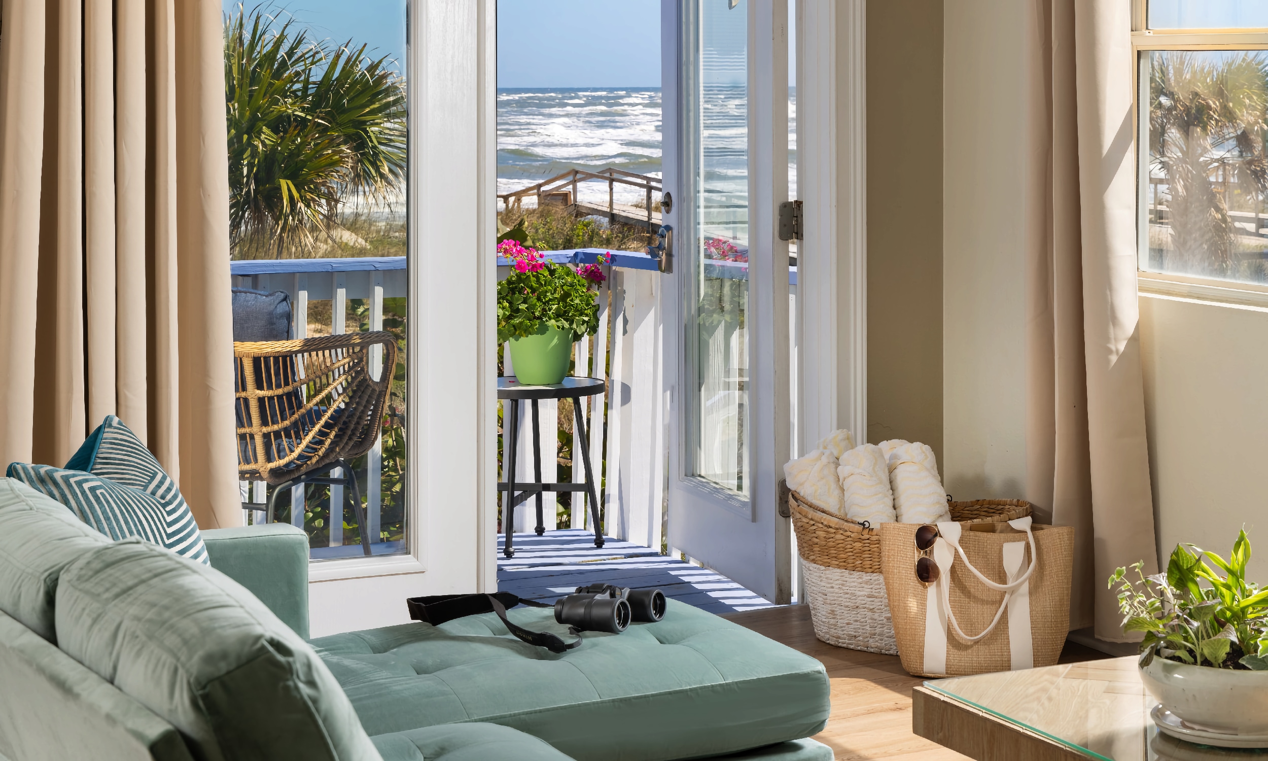 Looking beyond a soft teal-colored sofa in the forground, through the French doors to the private deck with a view of the Atlantic