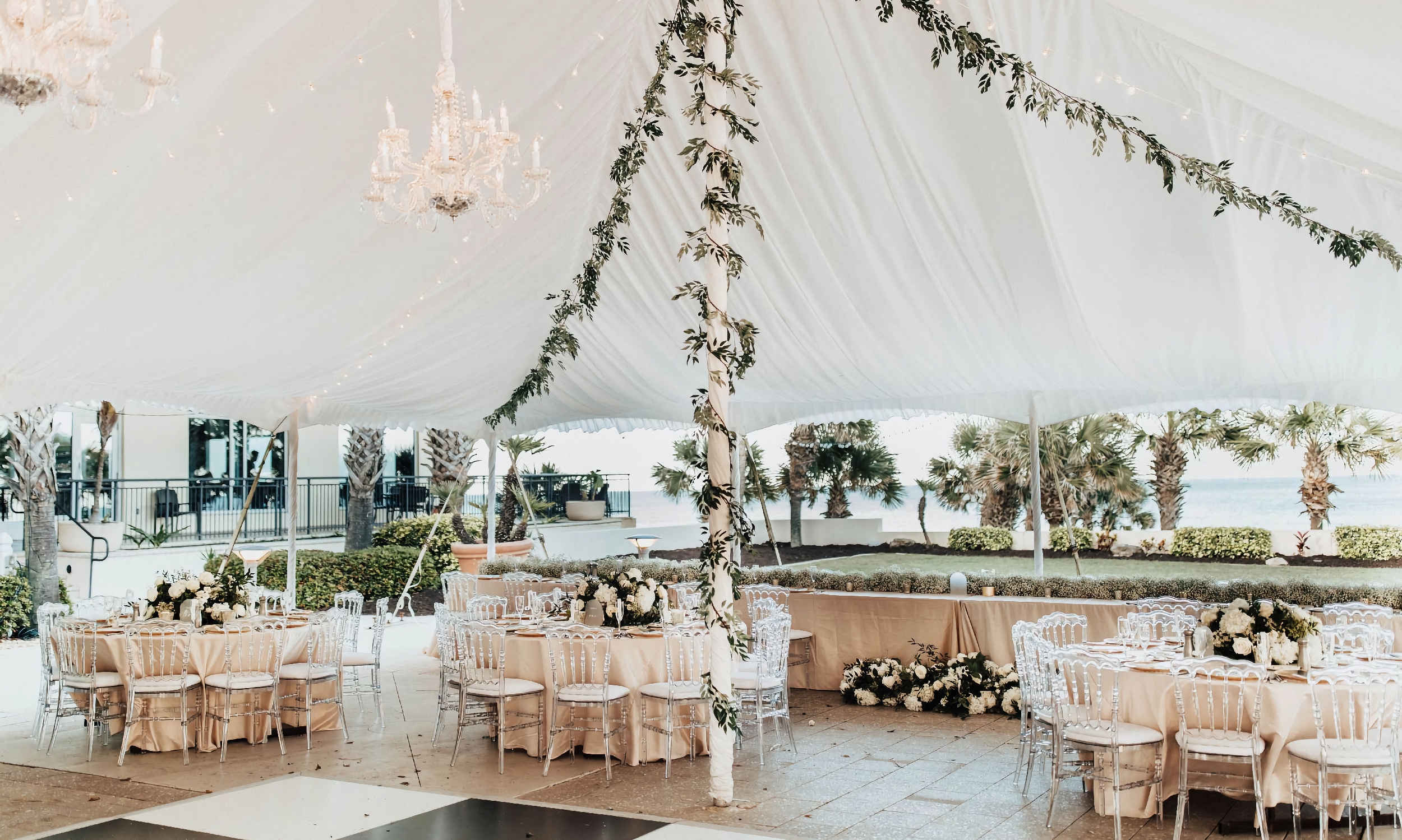 A wedding banquet with round tables and dance floor, under a decorated white tent