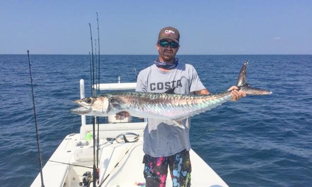 Man standing proudly on a boat, holding a large kingfish caught in St. Augustine