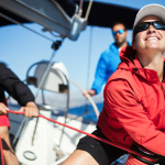 Three people sailing a sloop, a woman in the foreground at the winch