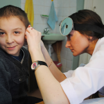 A young white boy getting his ear checked by a young white doctor. 