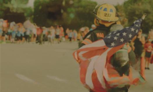 Race participant with American flag, wearing firefighter gear at the Tunnels to Towers 5K in St. Augustine