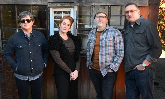 Bandmates from Six Pence None The Richer pose in front of a wooden window. 