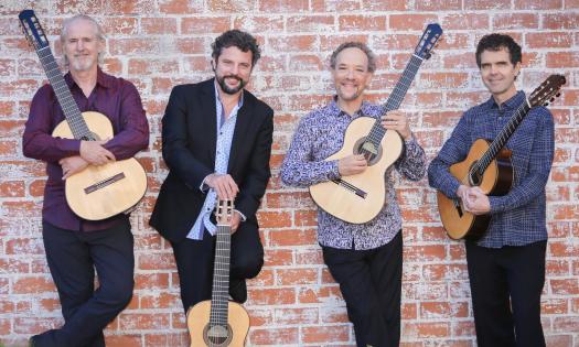 The Los Angeles Guitar Quartet, casually dressed and holding guitars while standing in front of a brick wall