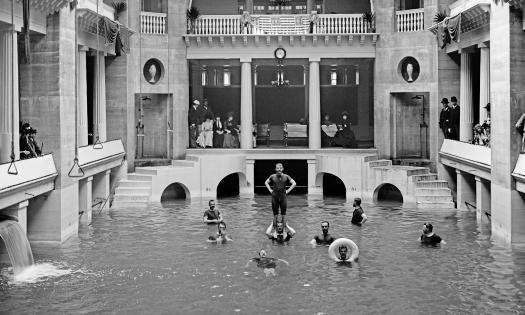 The Alcazar pool during the Gilded Age, with men exercising in the pool and people watching from the balcony