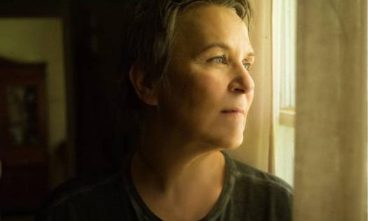 Mary Gauthier poses while peering out of an open window.