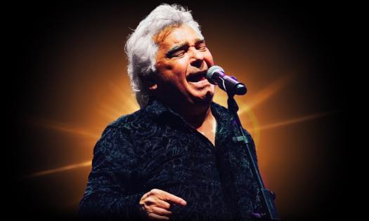 Nicholas Reyes wears black clothing while singing in front of a black and gold backdrop.