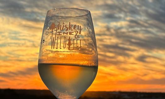 A wine glass, with white wine, raised to the sunset