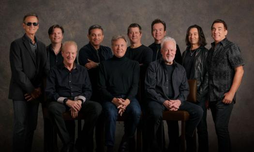 Bandmates from Chicago wear black and pose in front of a dark brown backdrop.