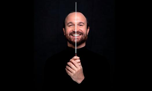 Composer and musician Juan Antonio Simarro in black, against a black backgroud, and holding a conductor's baton