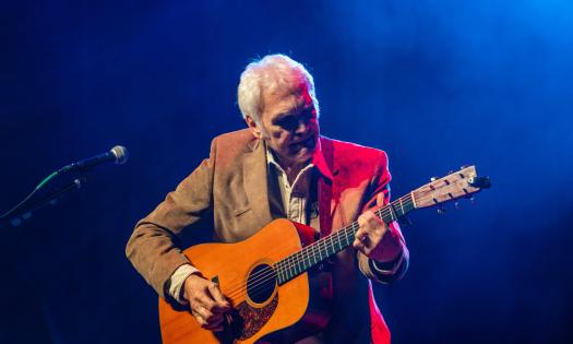 Verlon Thompson on stage with his guitar against a blue background