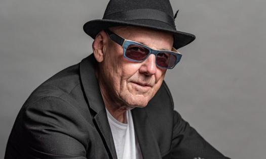 Billy Price stands against a gray backdrop, wearing black glasses and a coordinating fedora.