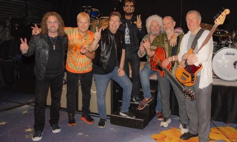 Bandmates from Ringo Starr and His All-Starr Band pose on stage with their musical instruments.