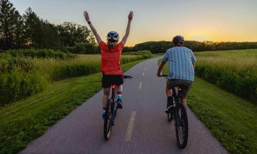 A couple seen from the back, riding on a bike path at sunset