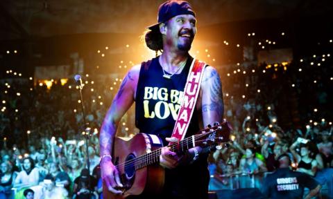 Michael Franti smiles while strumming his guitar. 