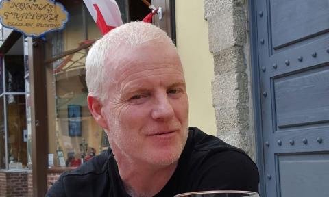 Derek Coghlan sitting an an outdoor cafe in St. Augustine, with a blue door in the background