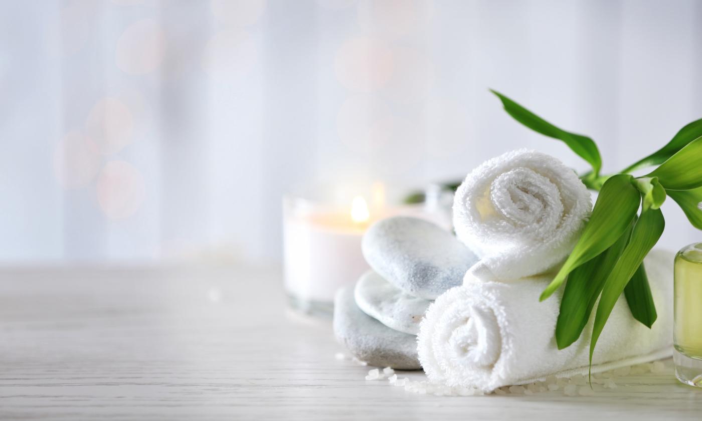 A cool white and green still life with a candle, folded towels, and greenery