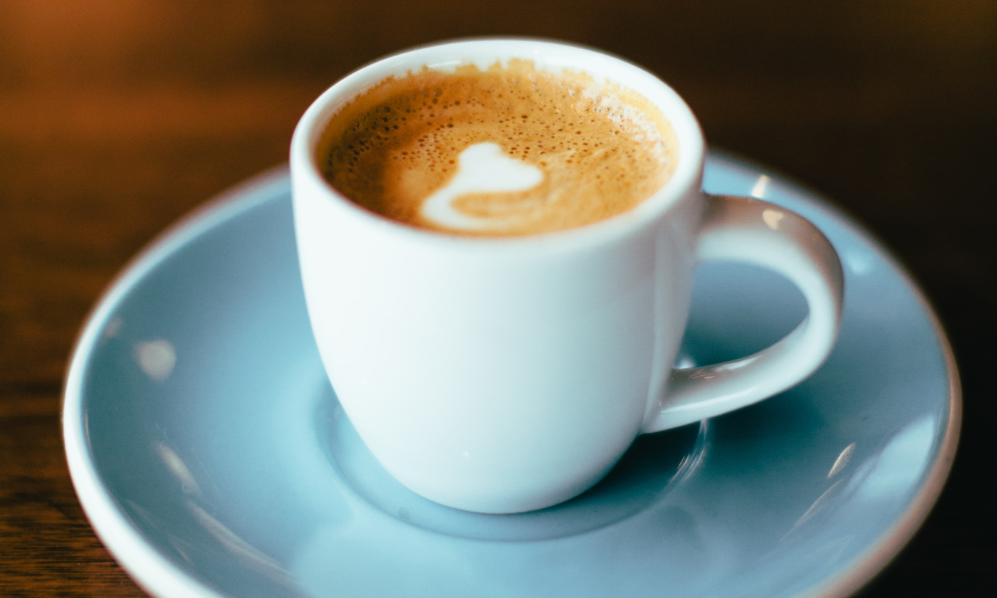 A cup of coffee sits on a blue plate. 