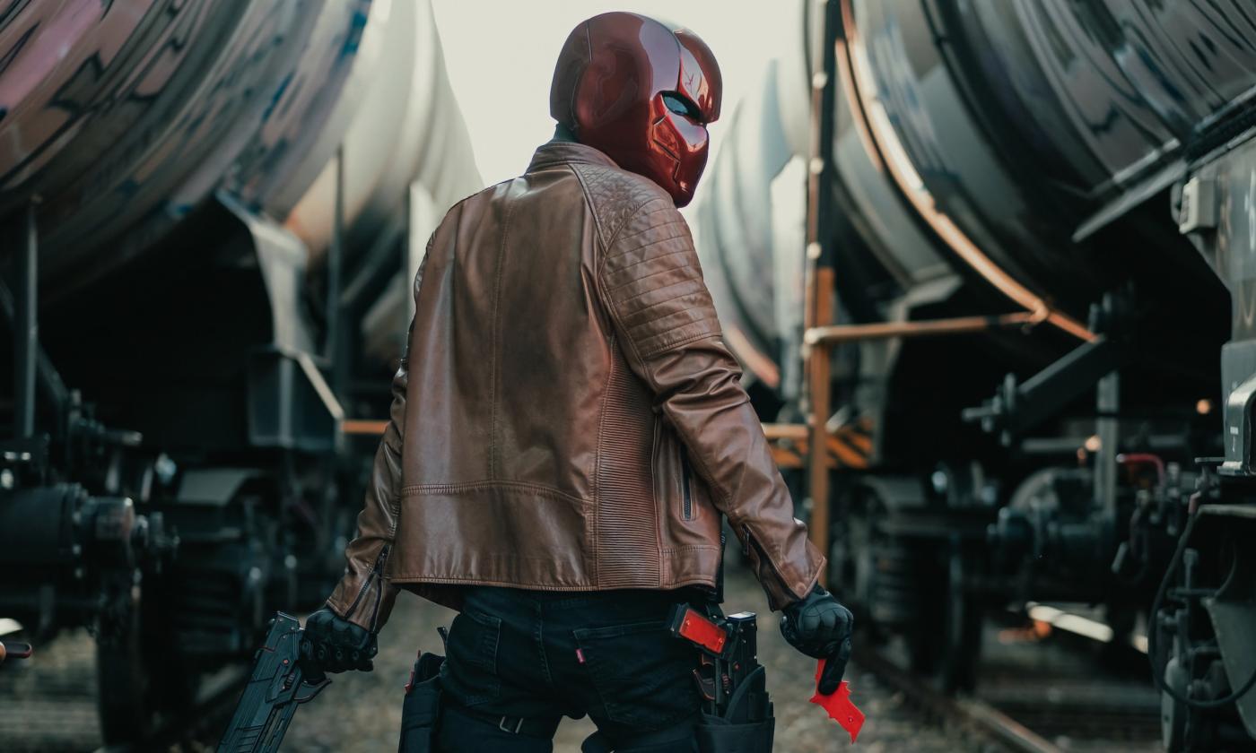 A man wears a mask and poses in front of a train.