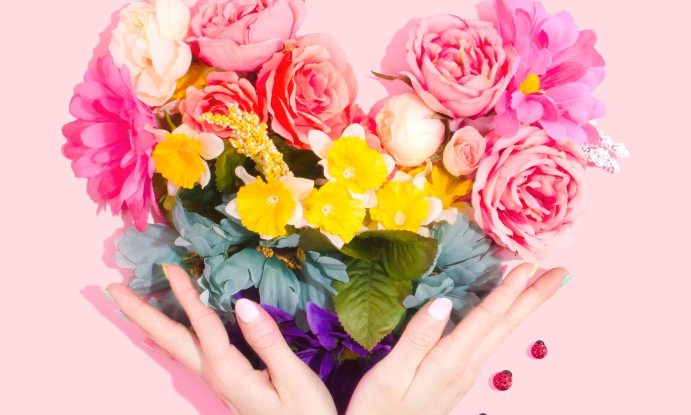 A colorful bouquet of flowers is held up by two hands