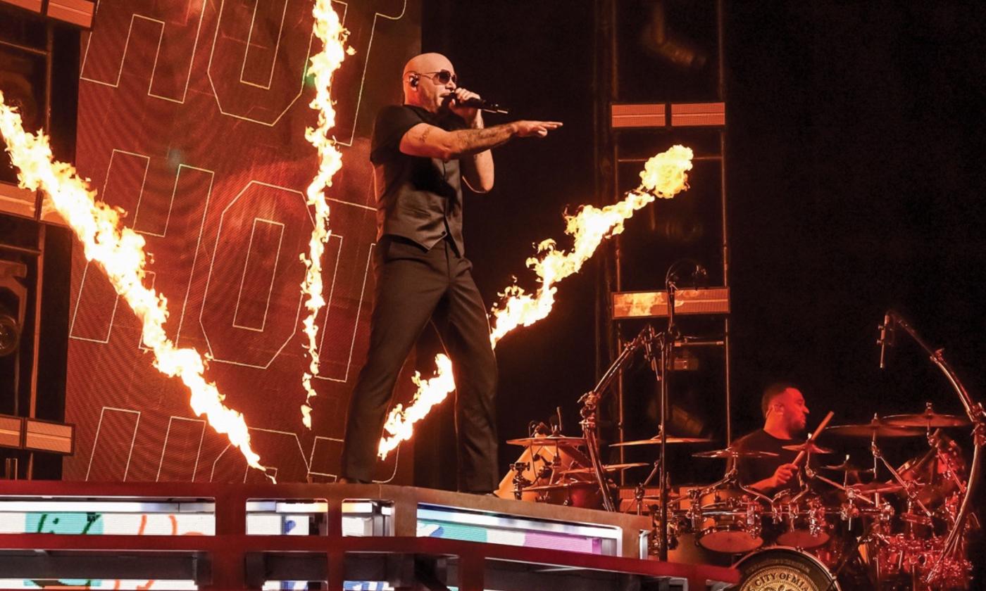 Pitbull performs on a stage with a fiery background