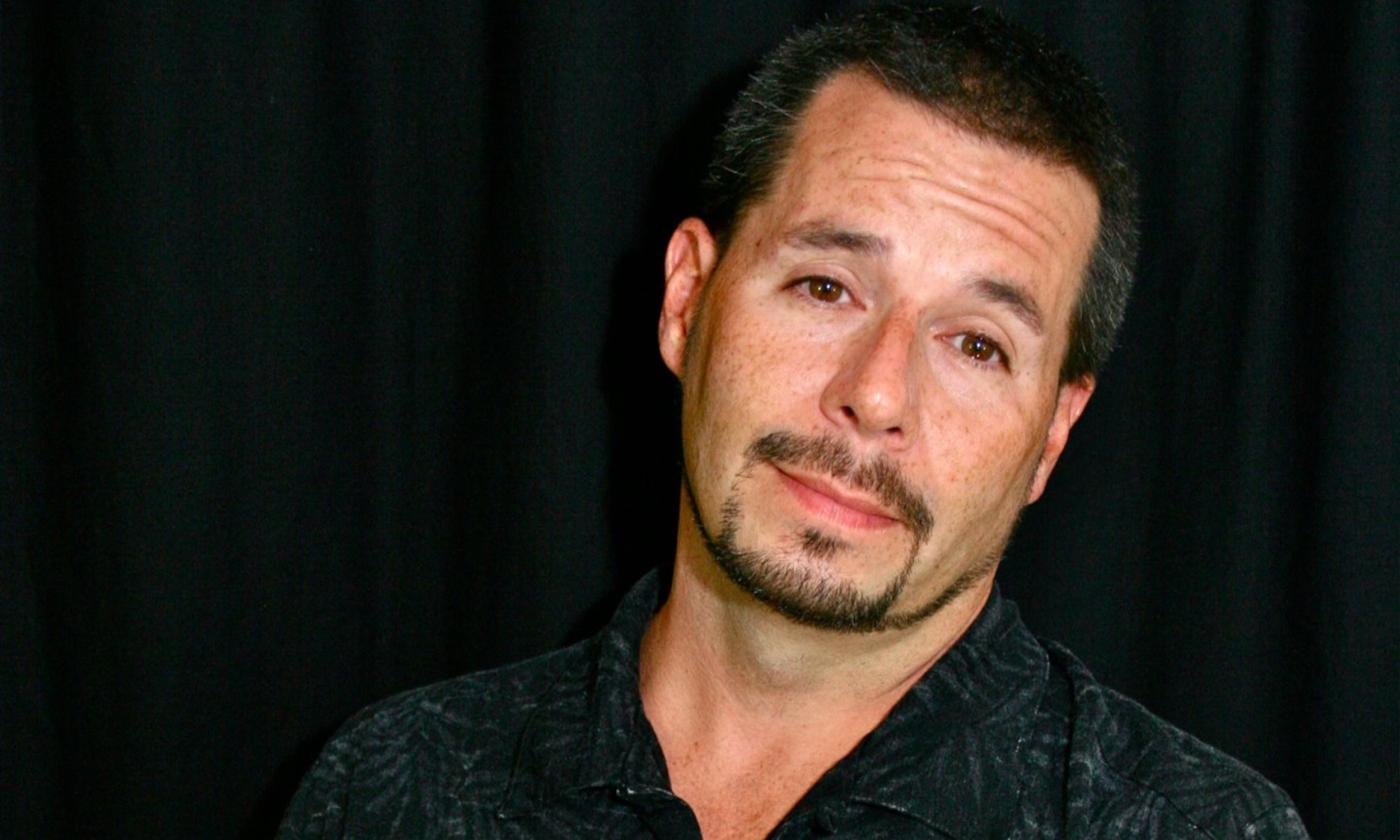 Tommy smirks with bright brown eyes and stands in front of a black background