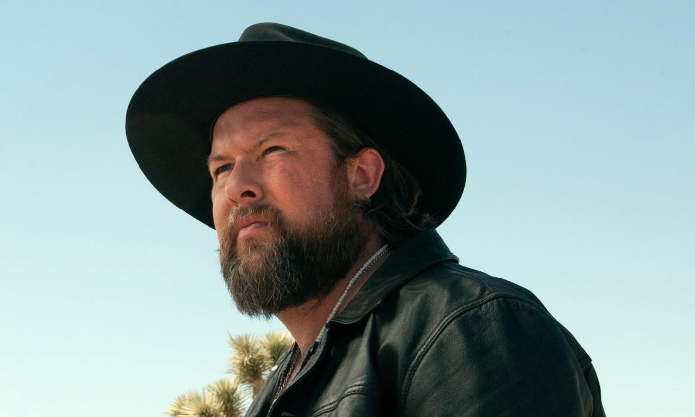 Zach William poses in a black hat and matching leather jacket.