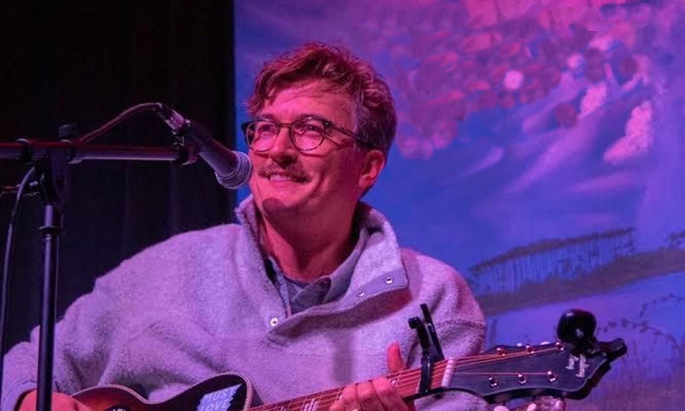 Songwriter Matt Dregstrem with guitar and microphone, smiling