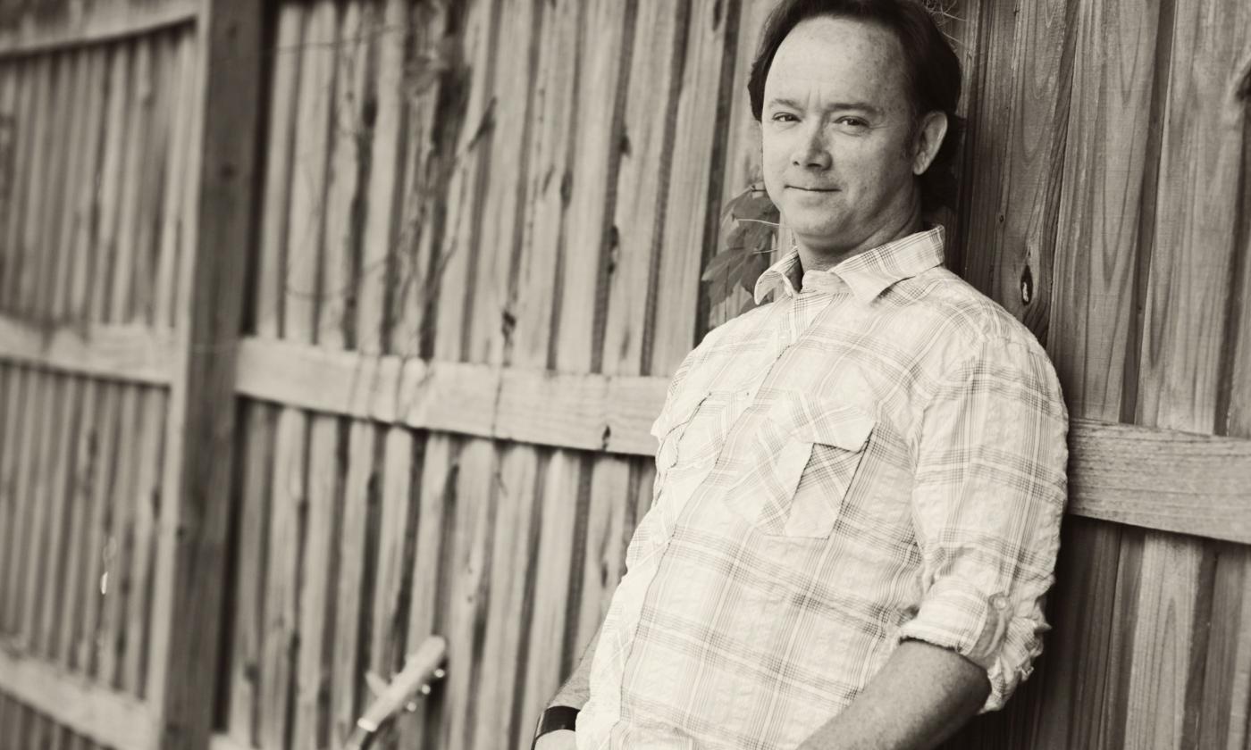 Musician Doug Burns, leaning against an old weathered stockaid fence