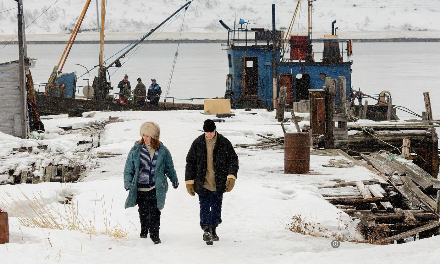 A scene from "Compartment No. 6," in which a man and a woman walk on a run-down dock in the Arctic circle