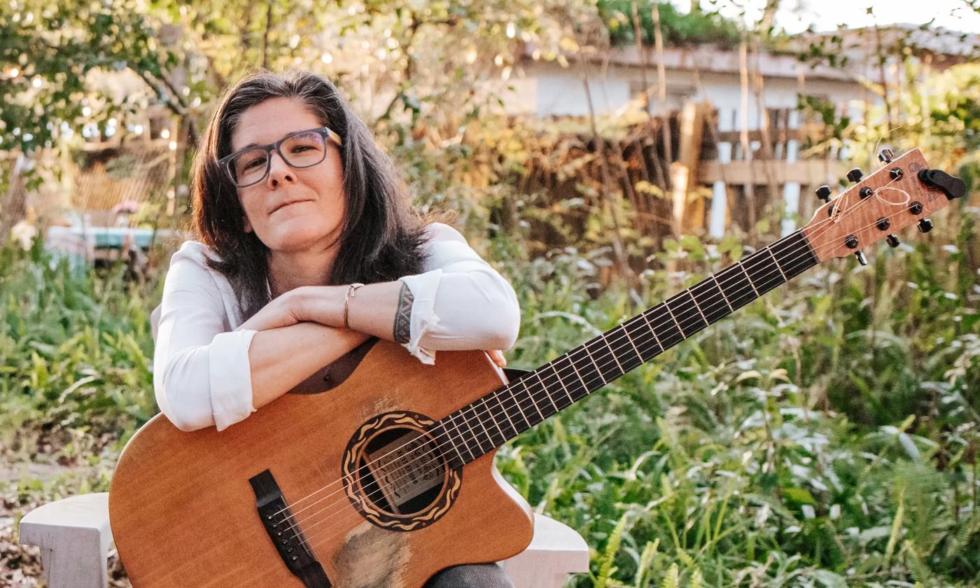 Singer/songwriter Chelsea Saddler in a garden with her battered guitar