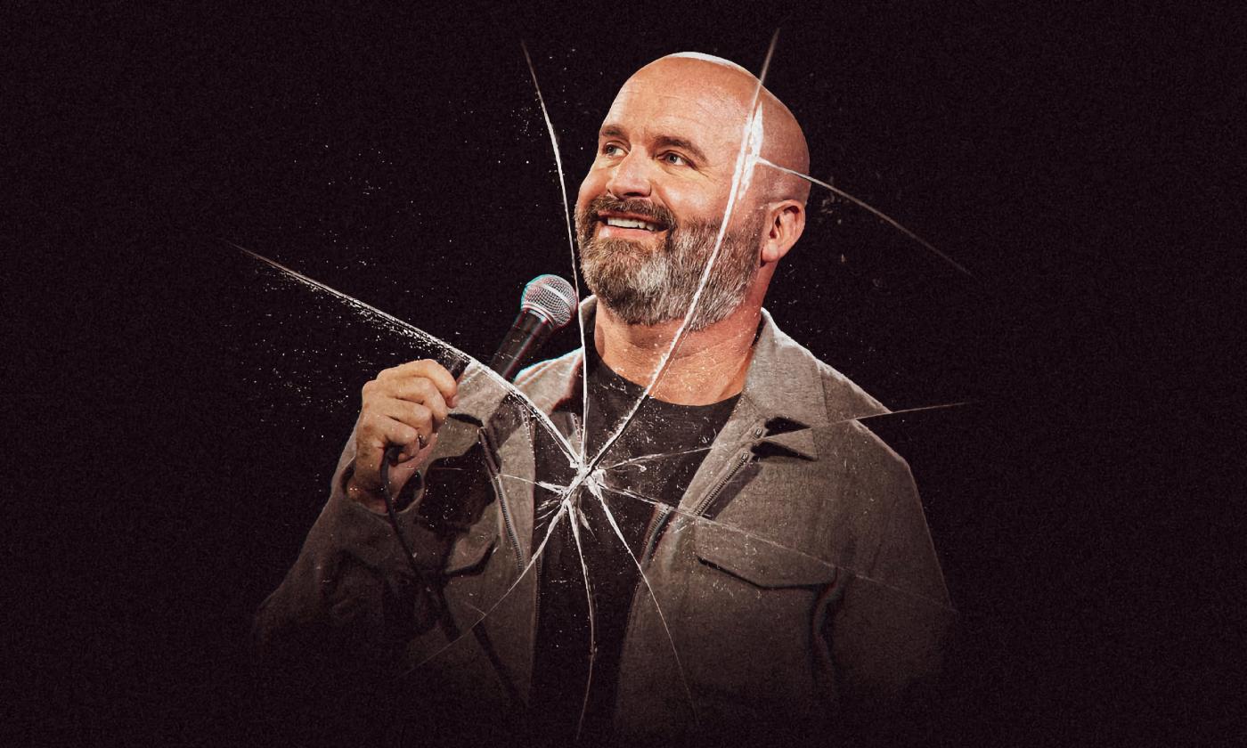 Tom Segura, with a microphone, in front of a "broken" camera